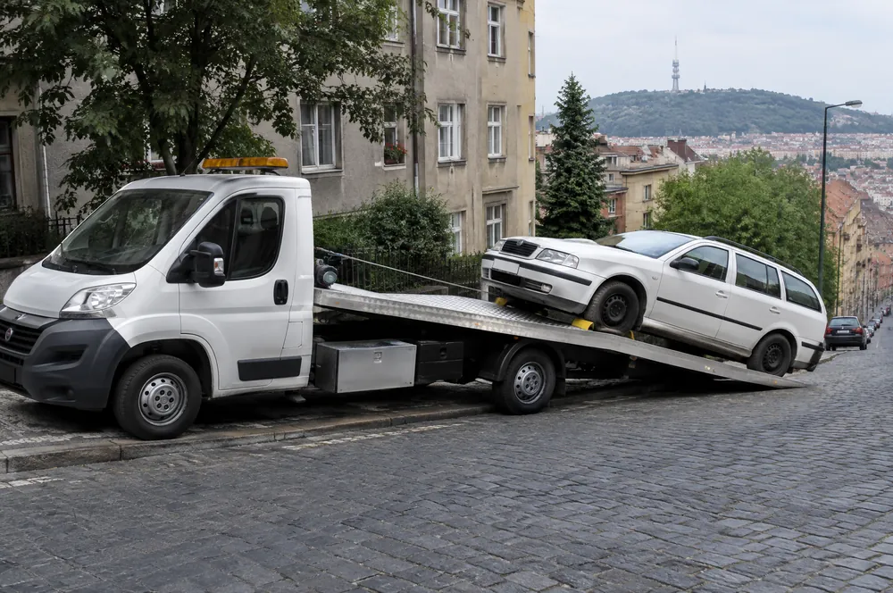 Naviják vytahuje bílou Škodu Octavii combi na plošinu odtahovky v prudké ulici pod Vítkovem