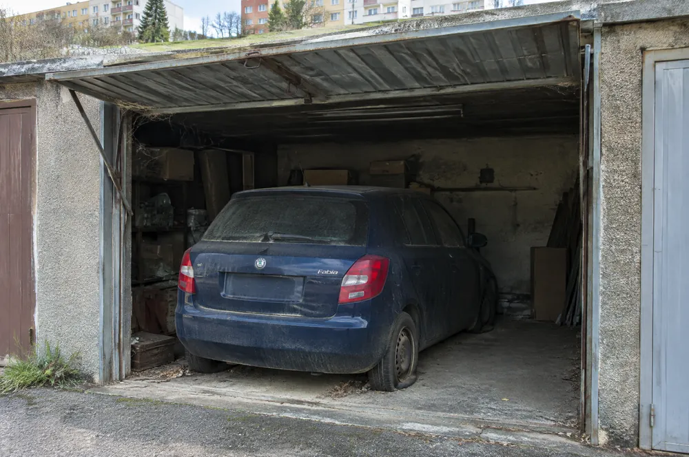 Zaprášená modrá Škoda Fabia s prázdnými pneumatikami stojí roky v řadové garáži na Vackově
